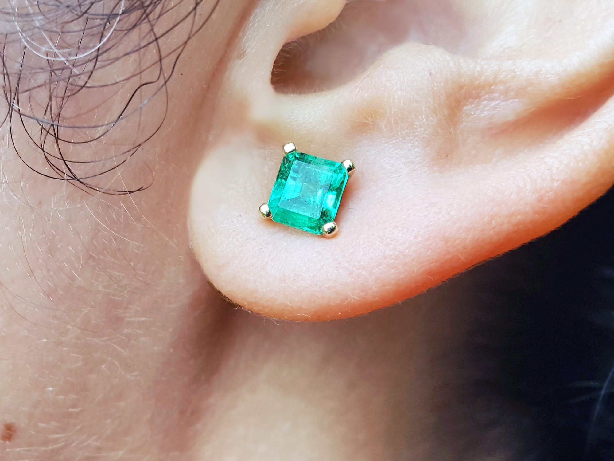 Close-up of an ascher cut emerald stud earring on an ear.