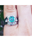 A men's emerald ring white gold on a finger against a natural background.