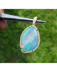 Opal pendant held by tweezers with a blurred green background.