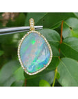 12.16 ct Australian opal pendant in 18K yellow gold, flashing bluish-green, held against leaves.