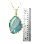 Opal pendant necklace with gold chain next to a ruler for size reference on a white background