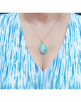Australian opal pendant with bluish-green play-of-color, handcrafted in 18K yellow gold, worn on a woman.