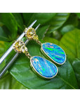 Opal earrings with gold accents on a green leaves background.