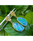 14K yellow gold dangle earrings with oval Australian opal doublets, bezel set, on a green leaf.