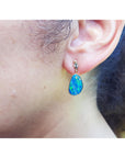 Close-up of an woman wearing a blue opal earring with a blurred background.