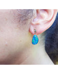Close-up of an woman wearing a blue opal earring with a blurred background.