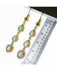 Gold earrings with natural Australian opal stones next to a ruler for size reference on a white background.