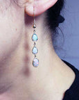 Close-up of a person wearing a set of opal earrings with a blurred background