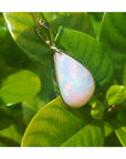 Pear-shaped Australian opal pendant with red-orange flashes in 14k yellow gold, on green leaves.
