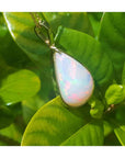 Pear-shaped Australian opal pendant with red-orange flashes in 14k yellow gold, on green leaves.
