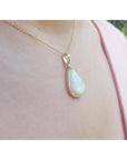 Teardrop-shaped pendant necklace on a person's neck against a blurred background.