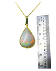 Pear-shaped Australian opal pendant with red-orange flashes in 14k yellow gold, next to a ruler.