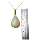 Pear-shaped Australian opal pendant with red-orange flashes in 14k yellow gold, next to a ruler.