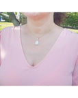 Pear-shaped Australian opal pendant with red-orange flashes on a 14k yellow gold chain, worn on a woman.