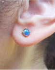 Round Australian opal doublet stud earring with blue play-of-color, prong-set in 14K gold on an earlobe.
