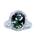 Australian sapphire ring for women oval cut with a sparkling bluish green hue, in a halo diamond crafted in 18K white gold.