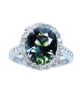 Australian sapphire ring for women oval cut with a sparkling bluish green hue, in a halo diamond crafted in 18K white gold.