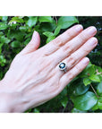 Hand wearing a 18k white gold ring with a blue sapphire against a green leafy background