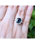 2.82 carat oval bluish-green Australian sapphire ring with diamond halo in 18K white gold on a hand.