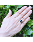 Oval bluish-green Australian sapphire ring with diamond halo, set in 18K white gold on a woman's hand.
