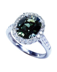 Oval bluish-green Australian sapphire ring with diamond halo and 18K white gold band.