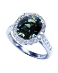 Oval bluish-green Australian sapphire ring with diamond halo and 18K white gold band.