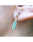 Close-up of a 14K gold baggette cut emerald stud earring worn on an ear.