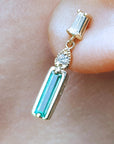 Dangle baguette cut emerald stud earrings on a person's ear