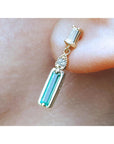 Dangle baguette cut emerald stud earrings on a person's ear