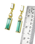 A pair of yellow gold Baggette cut emerald stud earrings next to a ruler for size measure.