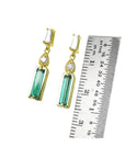 A pair of yellow gold Baggette cut emerald stud earrings next to a ruler for size measure.