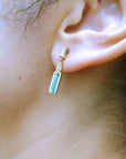 Close-up of an ear wearing yellow gold baggette cut emerald stud earrings with a blurred background