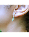 Close-up of an ear wearing yellow gold baggette cut emerald stud earrings with a blurred background
