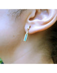 14K gold stud earring with baguette emerald, pear-shaped diamond, and tapered baguette diamonds.