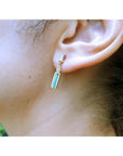 14K gold stud earring with baguette emerald, pear-shaped diamond, and tapered baguette diamonds.
