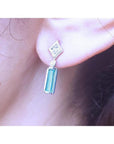 14K white gold emerald baguette and diamond stud earrings on an ear.