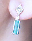Close-up of a white gold emerald earring with accent diamonds worn on an ear.