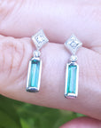 Pair of emerald white gold earrings held between fingers against a blurred background