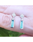 Pair of emerald white gold earrings held between fingers against a blurred background