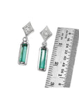 Pair of earrings with natural emeralds and diamond tops next to a ruler for scale on a white background