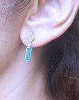 Close-up of an ear wearing a diamond and emerald earring with blurred background