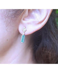 14K white gold emerald baguette cut earrings with diamond studs on an ear.