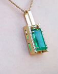 Gold pendant with a baguette cut emerald gemstone on a person's chest.