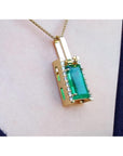 Gold pendant with a baguette cut emerald gemstone on a person's chest.