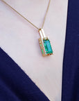 Gold necklace with a natural emerald pendant on a white and person's neck.
