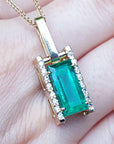 Gold pendant with a baguette cut emerald held on hand.