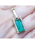 Gold pendant with a baguette cut emerald held on hand.