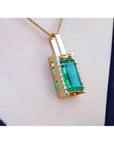 Gold pendant with a rectangular baguette cut natural colombian emerald gemstone on a person's chest.