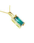 Baguette cut Colombian emerald pendant in 18K yellow gold with diamond accents on a delicate chain.