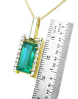 Gold pendant with a baguette cut emerald next to a ruler for scale on a white background.